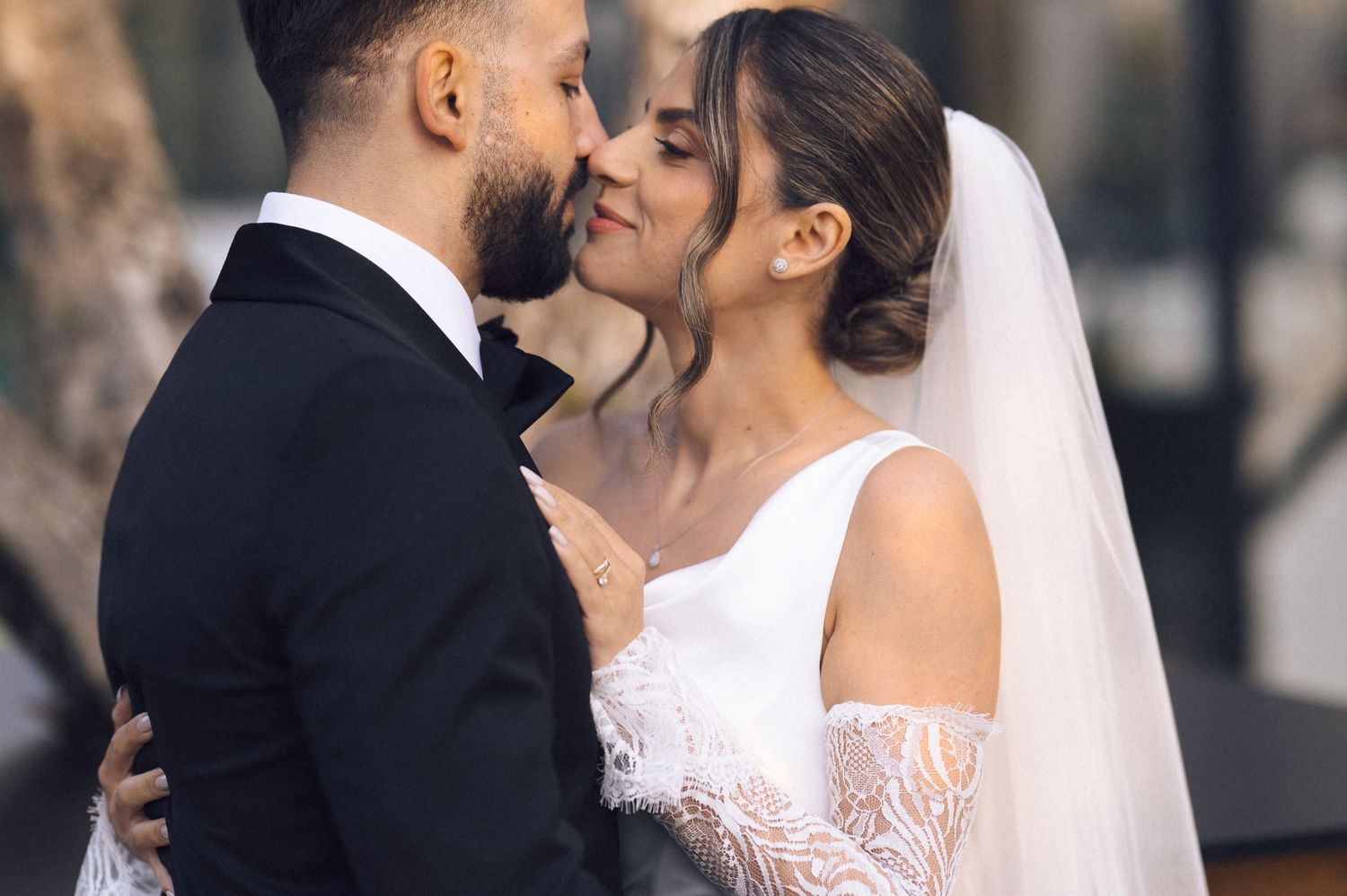 Bride and groom sharing a romantic almost-kiss moment on their wedding day, wearing elegant white gown and black tuxedo.