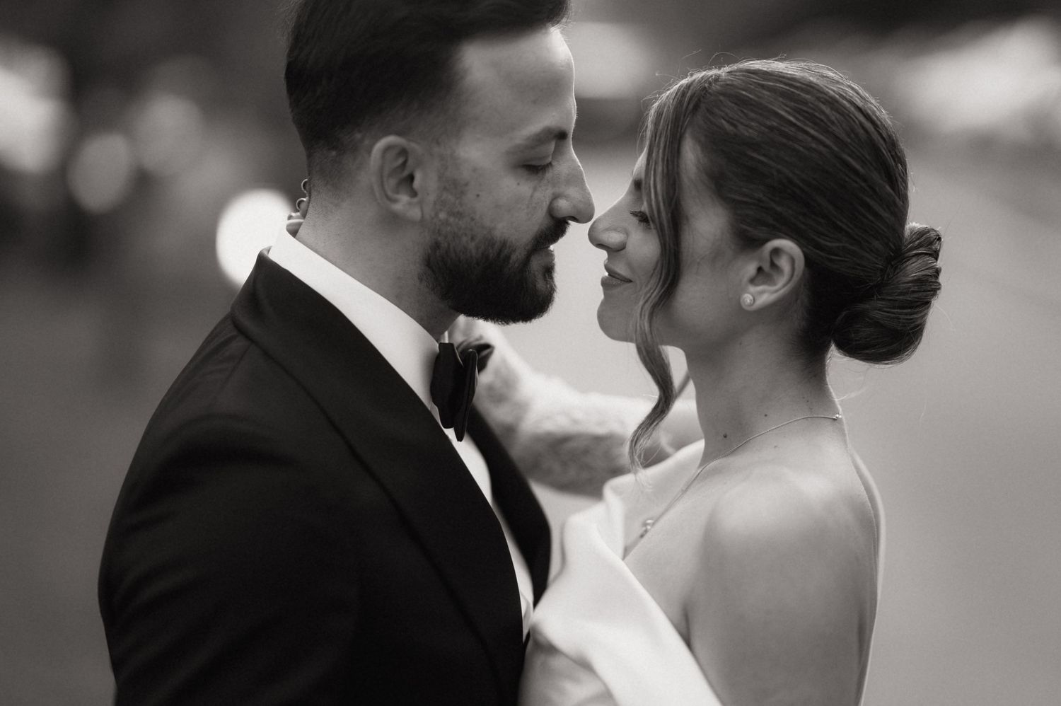 Black and white wedding photo of bride and groom sharing an intimate moment, almost kissing, dressed in formal attire.
