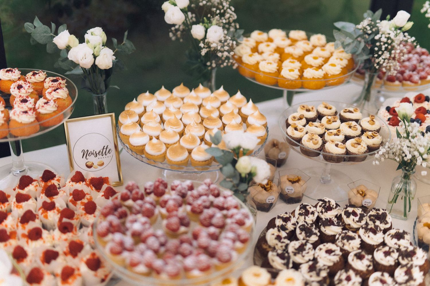 Elegant wedding dessert table with cupcakes, macarons, and petit fours arranged on tiered stands with floral decor.