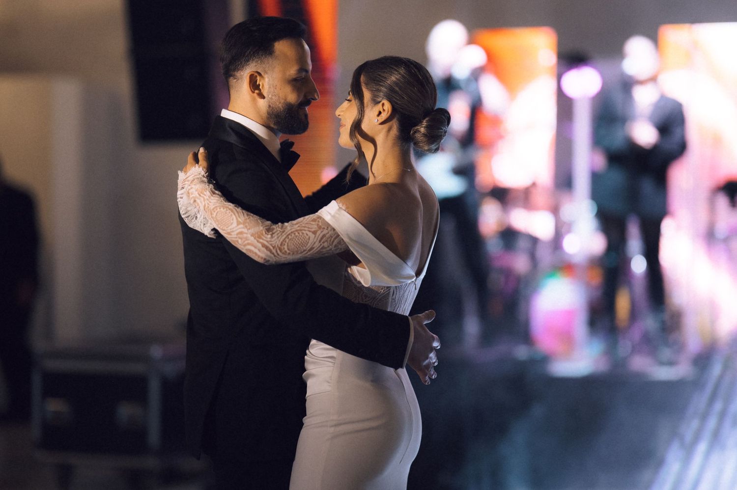 Bride and groom share first dance at wedding reception with live band performing on stage in background.