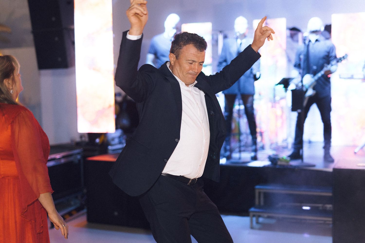 Man dancing energetically at a party event with a live band performing on stage in the background.