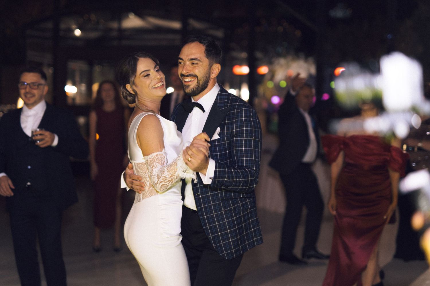 Bride and groom share first dance at elegant wedding reception, bride in white gown, groom in plaid suit.