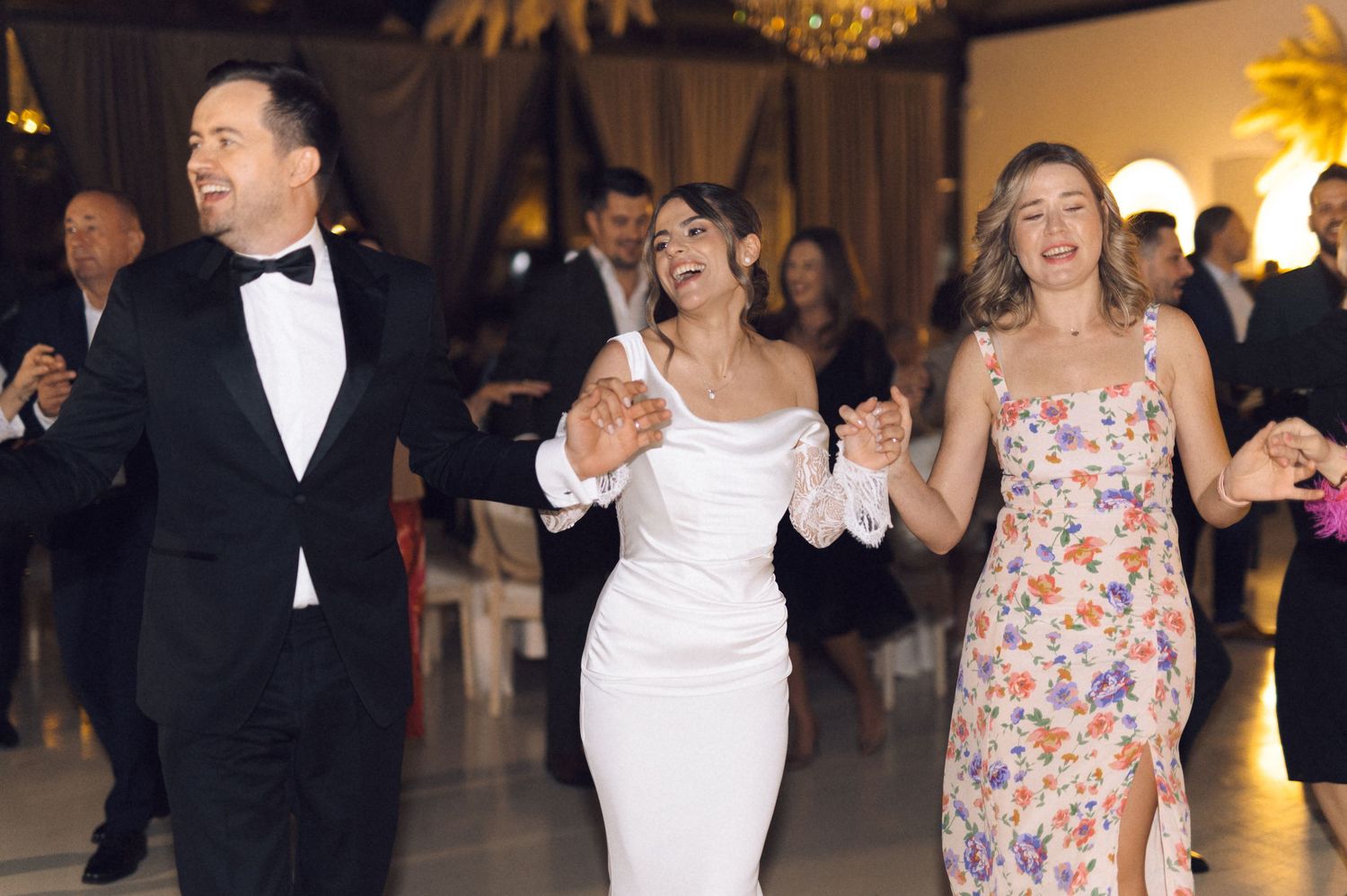 Bride in white gown dancing joyfully with guests in formal attire at an elegant wedding reception.