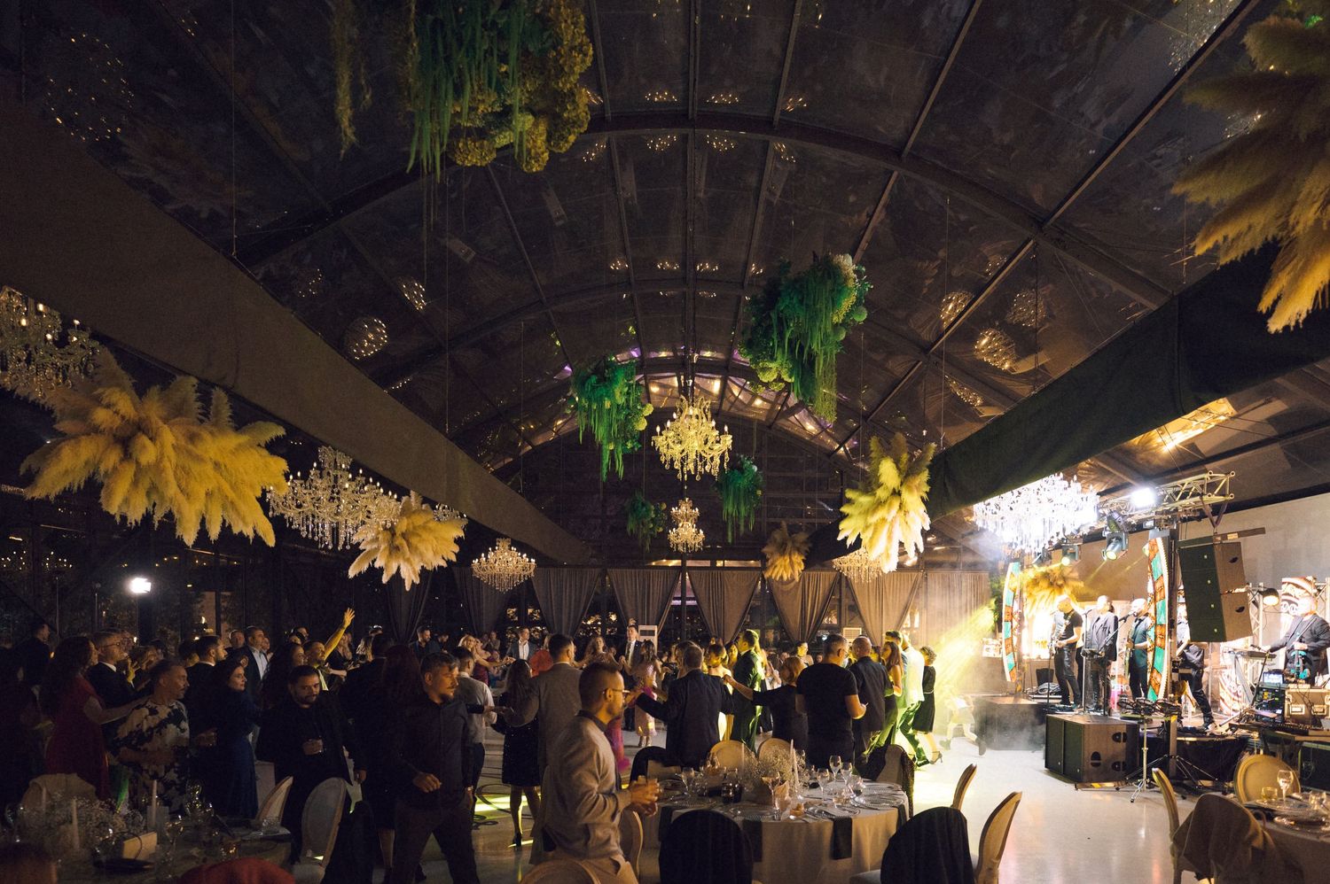 Elegant indoor gala event with yellow floral ceiling decor, chandelier lighting, and guests mingling at decorated tables.