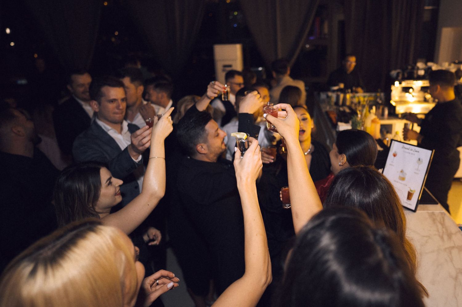 Guests at an upscale evening event raising phones and cameras to capture a moment at a dimly lit venue.