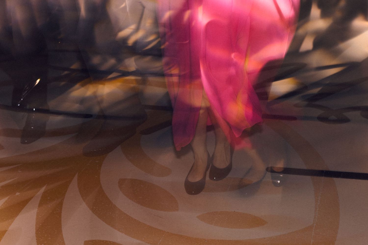 Blurred motion shot of a woman in a pink dress dancing, with swirling light patterns on the floor.