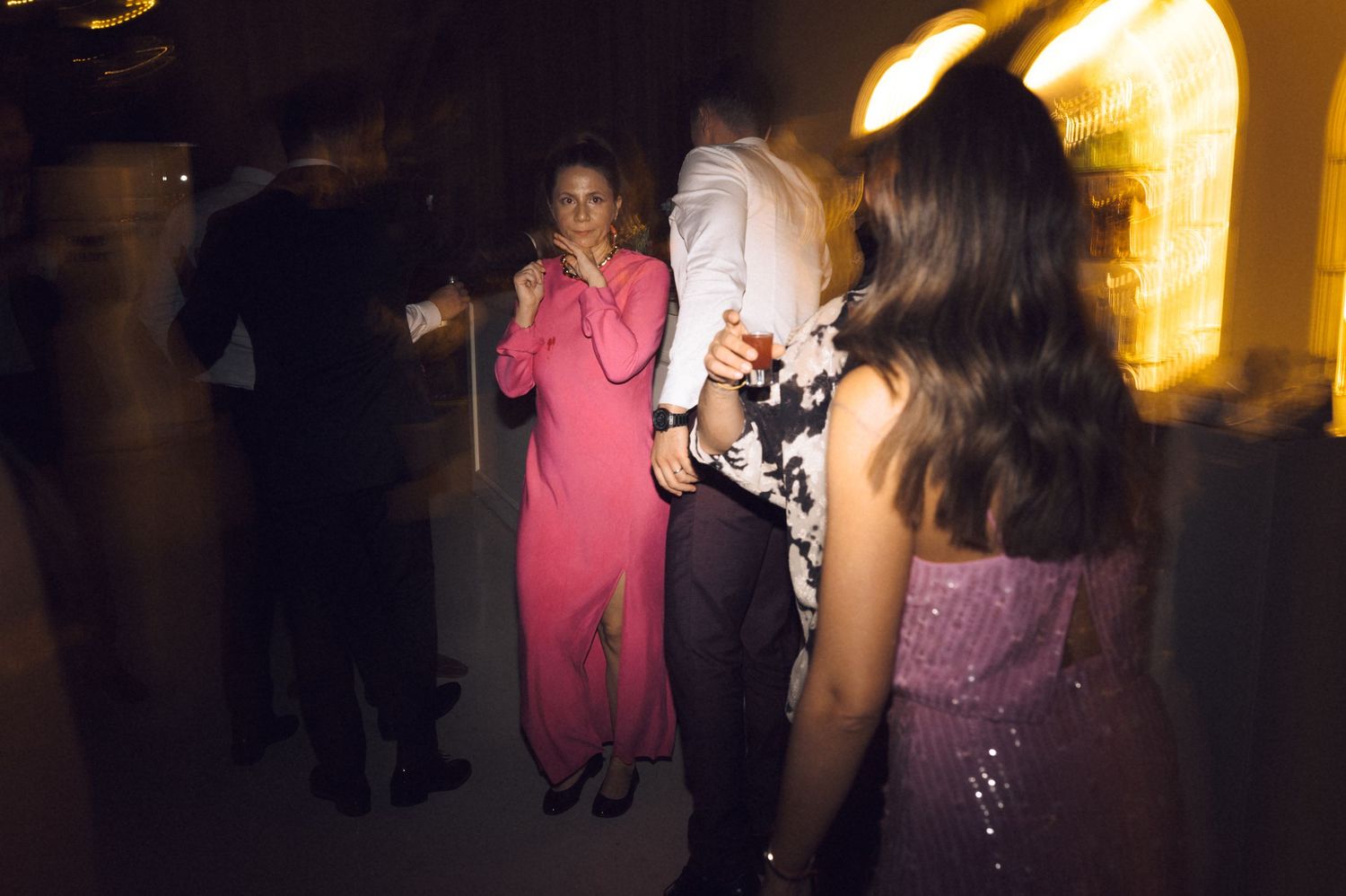 Guests in elegant attire dance at a formal evening party, featuring a woman in a pink gown.