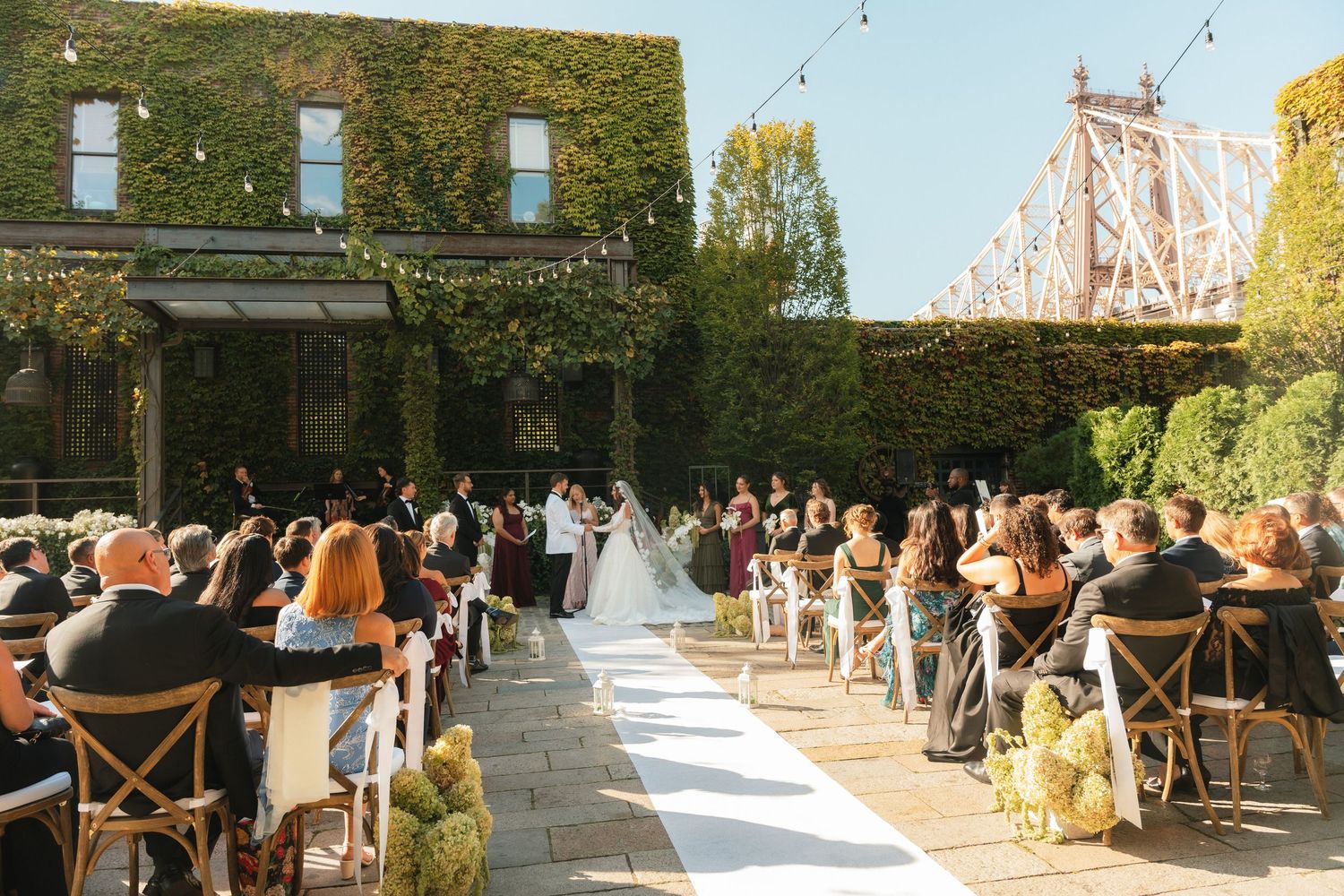 Outdoor wedding ceremony setup with ivy-covered walls and string lights creating an enchanting atmosphere.