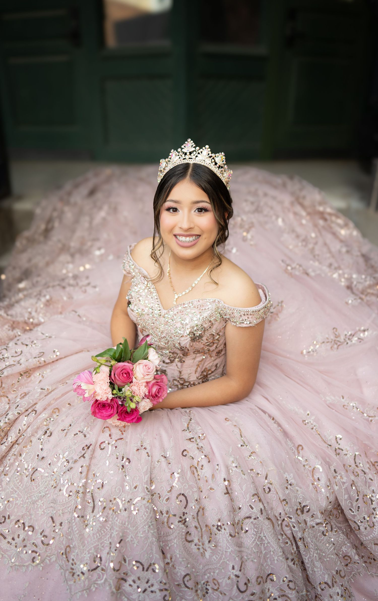 Figure in a voluminous sparkly blush ballgown poses at sunset near a classic building with dramatic train and lighting.