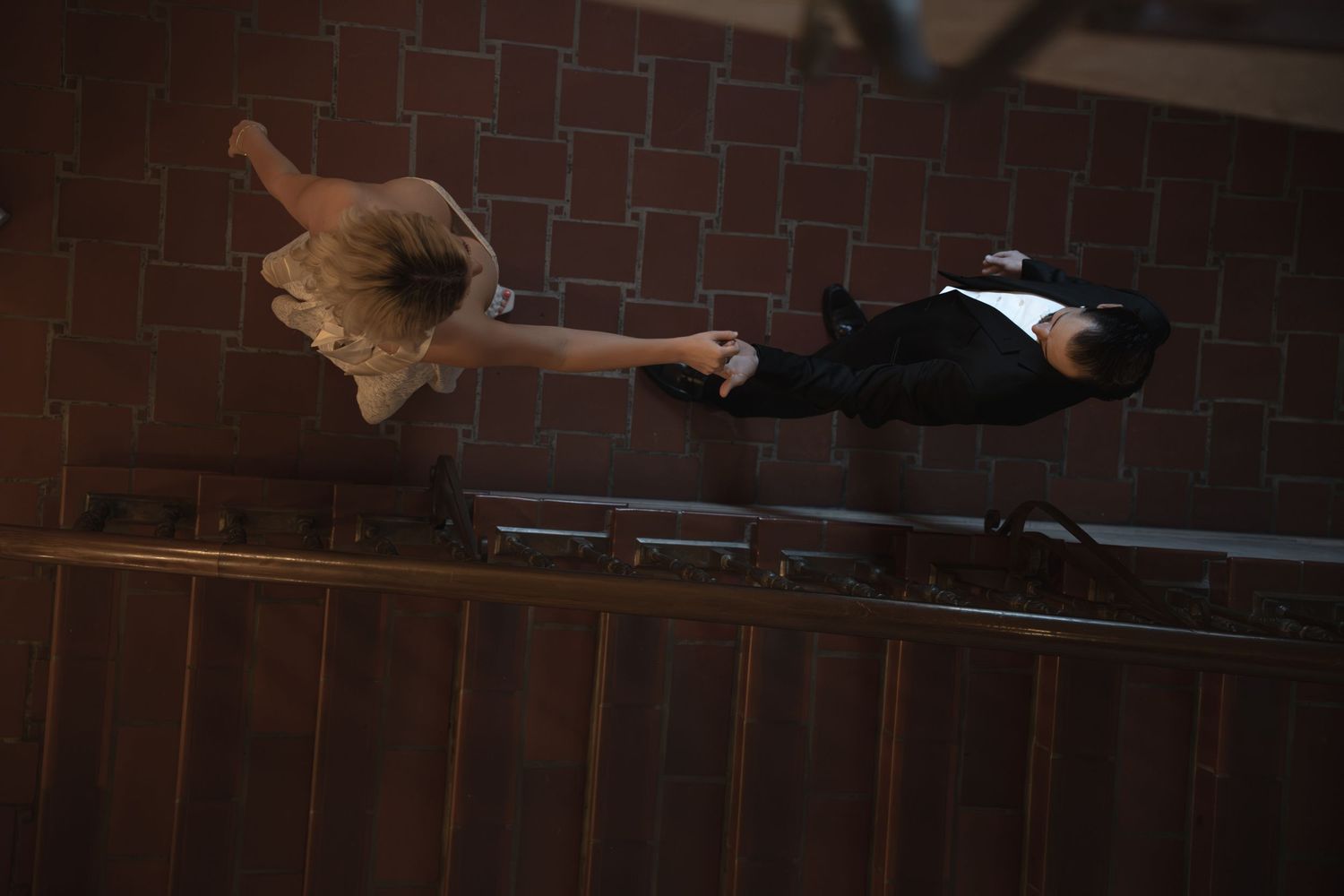 Aerial view of a couple in formal attire holding hands while walking along a staircase railing.