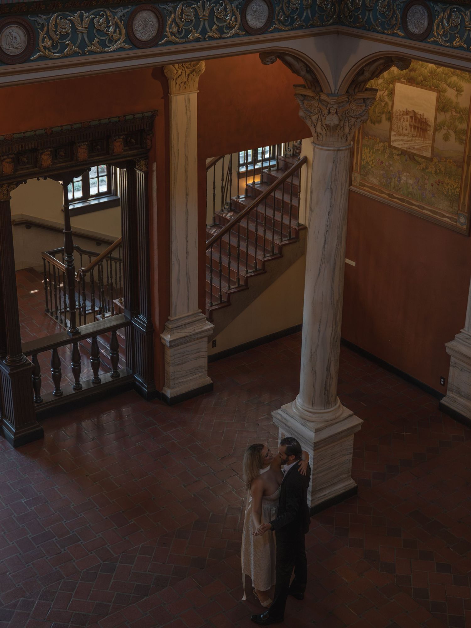 Couple sharing a romantic moment beneath ornate marble columns in a grand historic building interior.