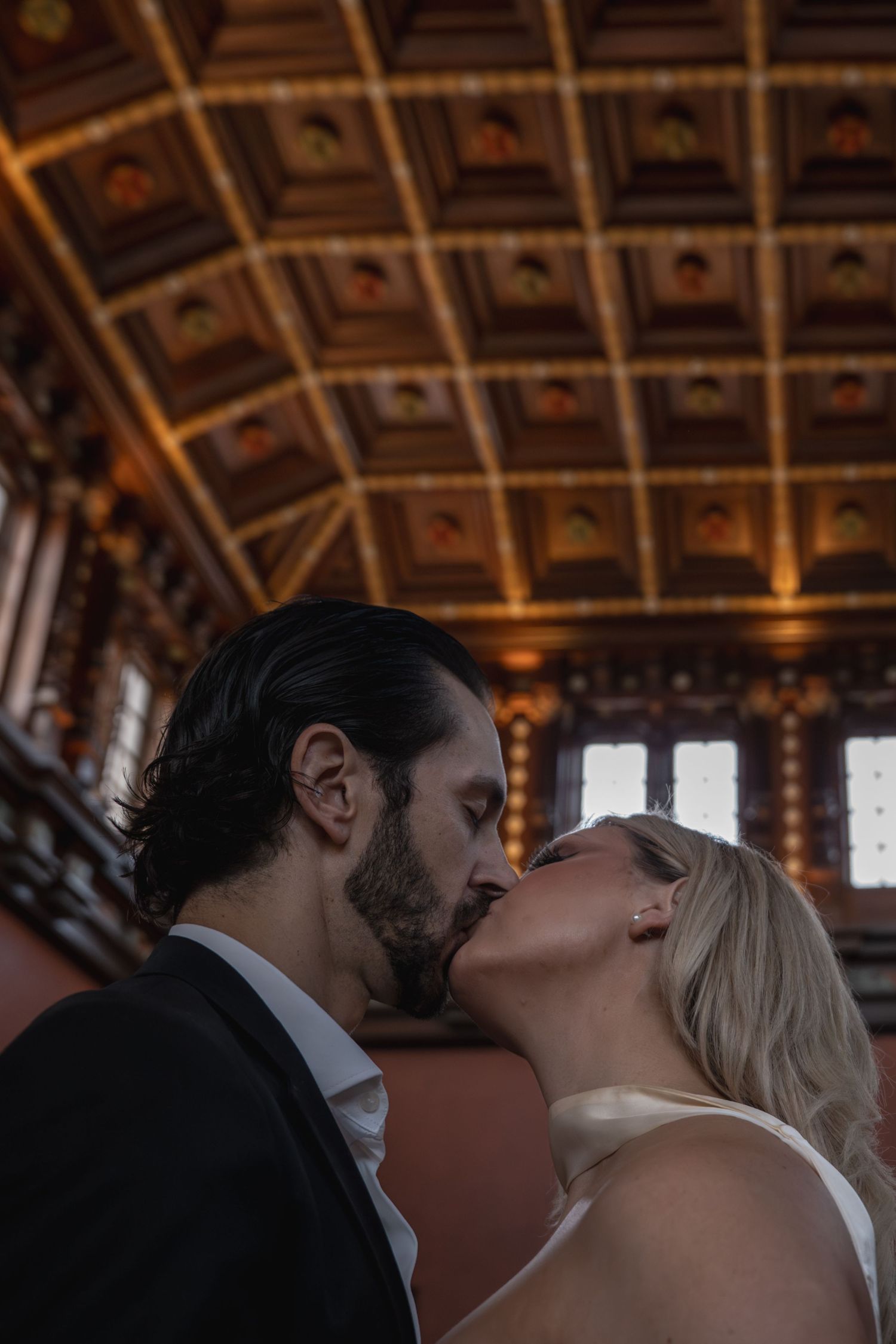 Couple sharing a passionate kiss beneath an ornate gilded ceiling in a stunning historic venue.