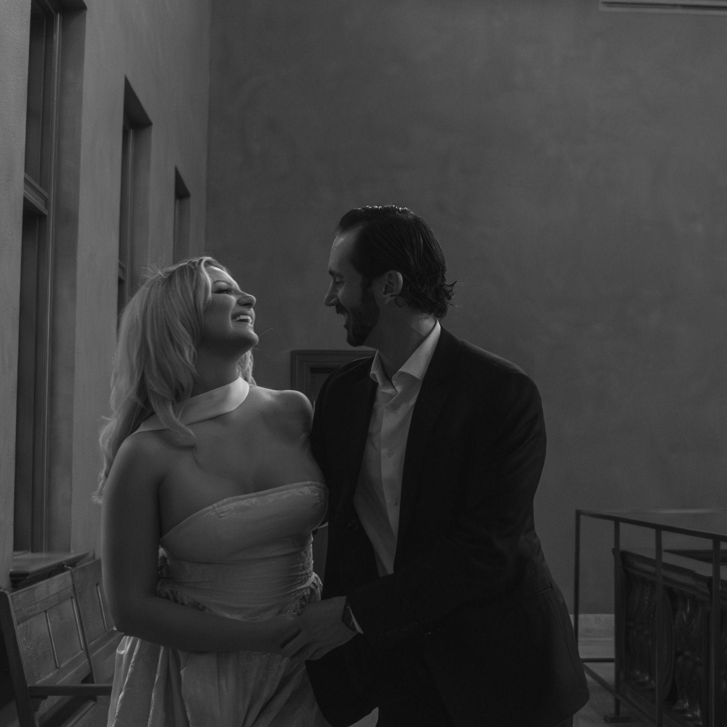 Black and white photo of smiling couple embracing outdoors in romantic moment.