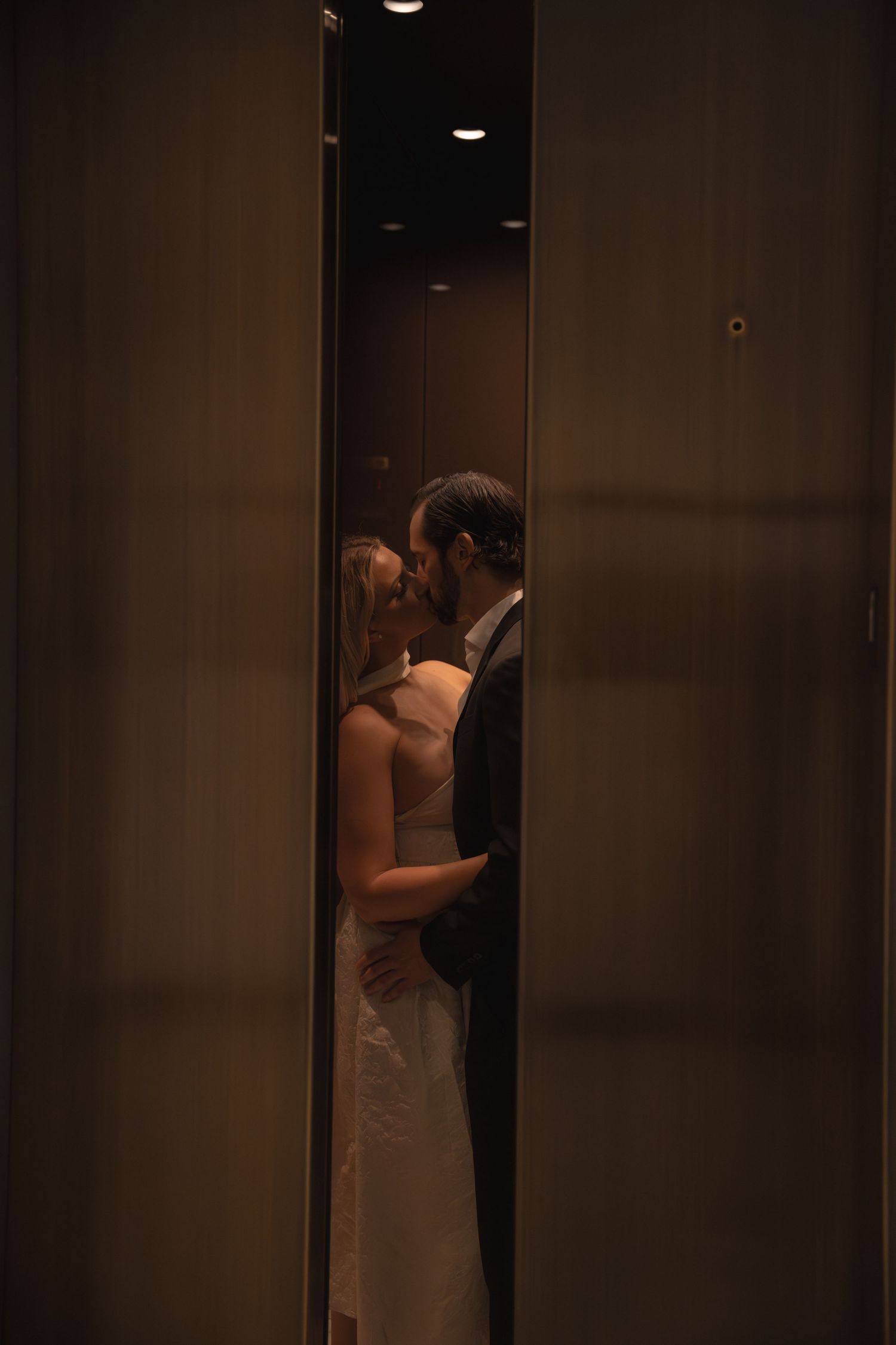 Couple sharing a kiss inside elevator seen through narrow opening of closing doors.