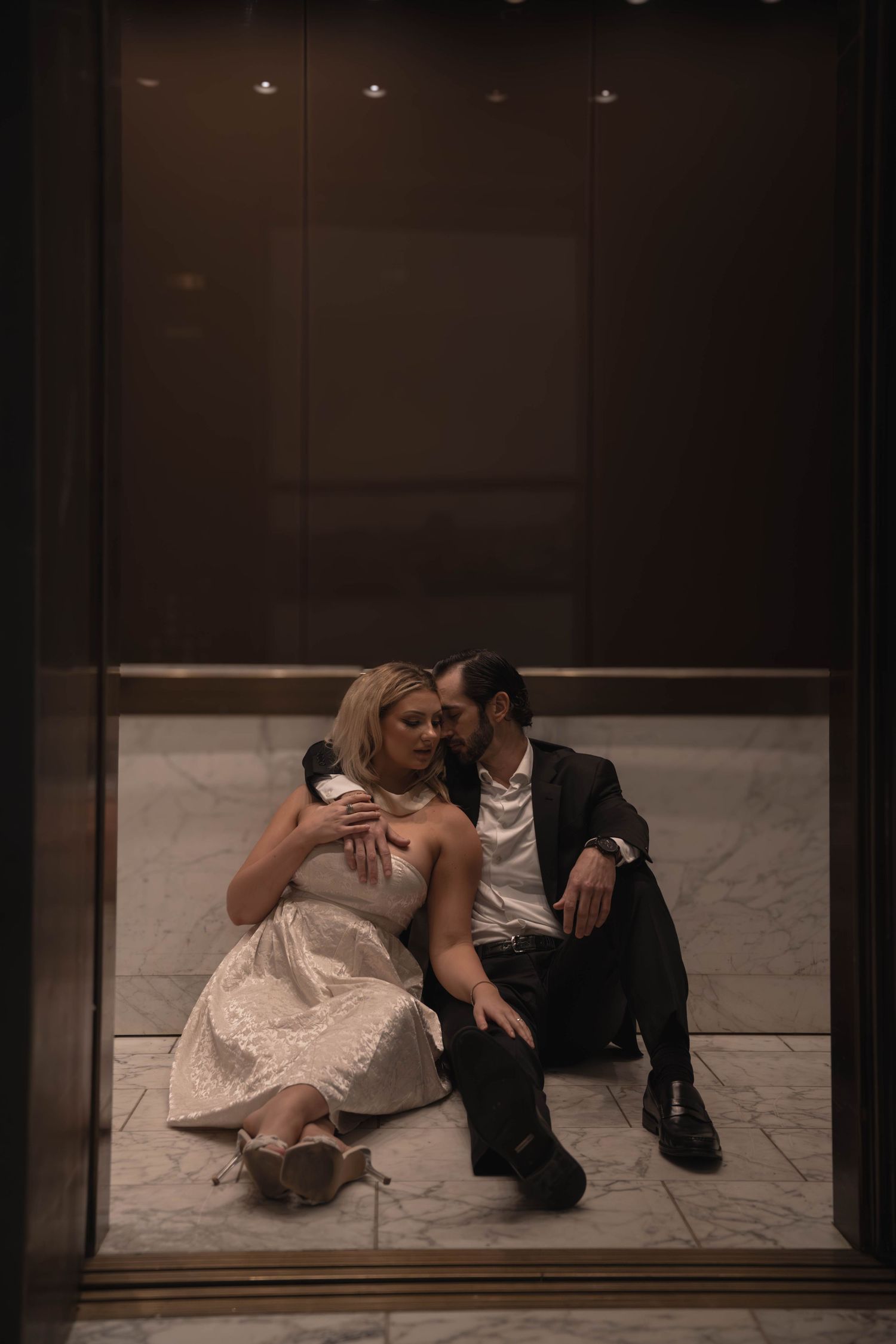 Bride and groom sitting on elevator floor in an intimate and candid wedding portrait.