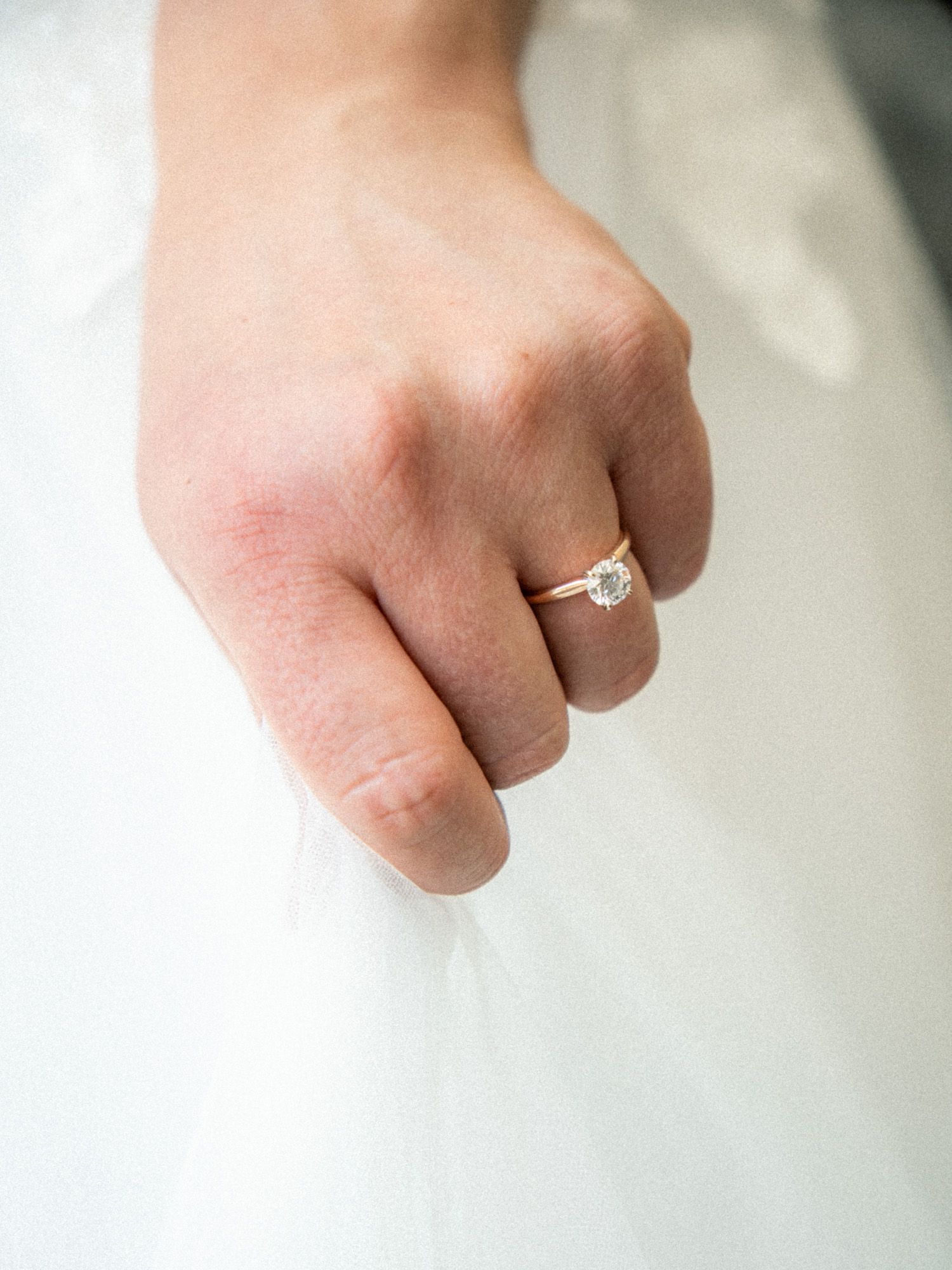 Close-up view of a hand wearing a sparkling diamond engagement ring on white fabric background.