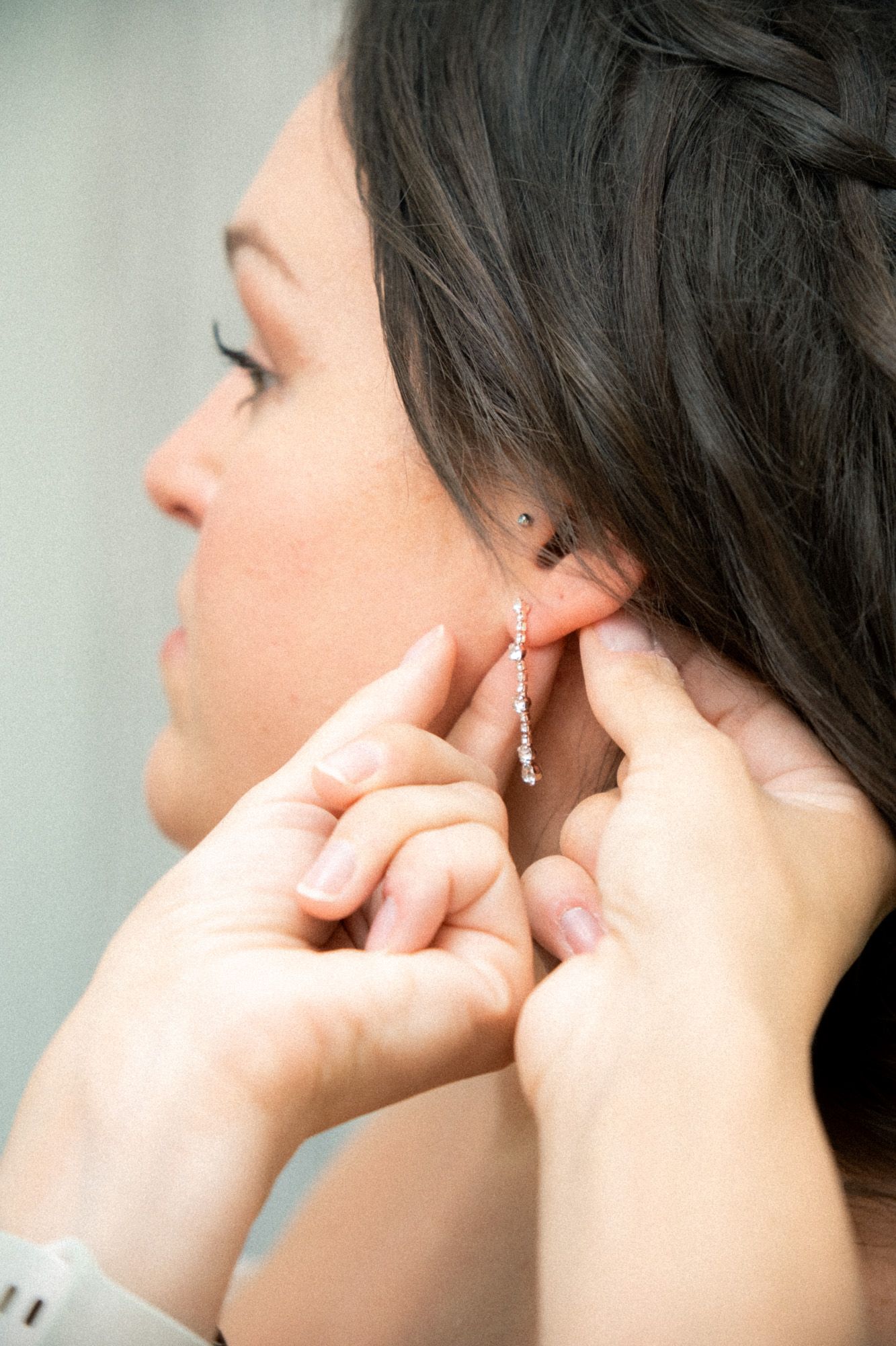 Hands carefully fastening a delicate crystal drop earring during wedding preparations.