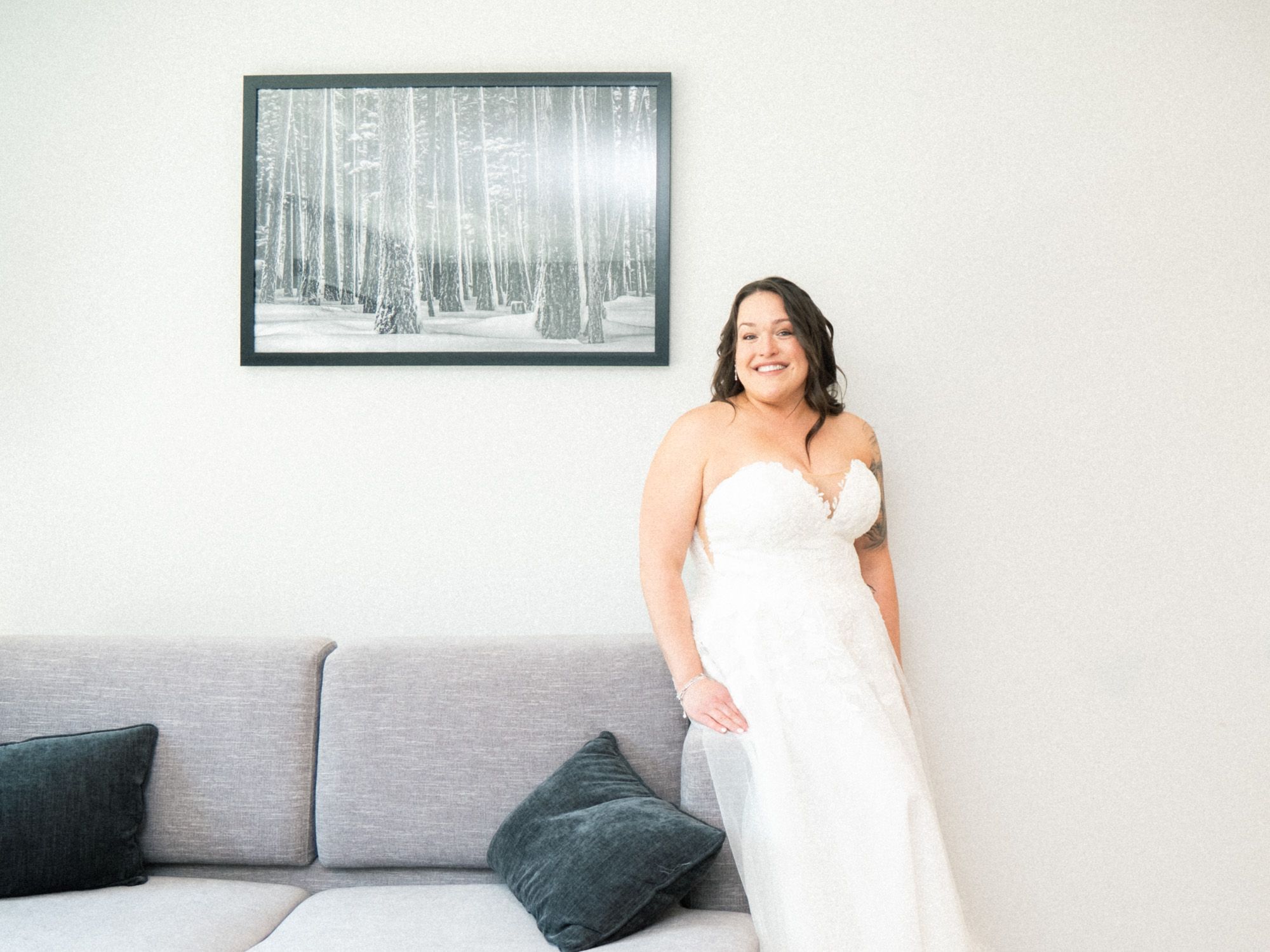 A person in a white dress sits on a grey couch in a modern living room with framed artwork on the wall.
