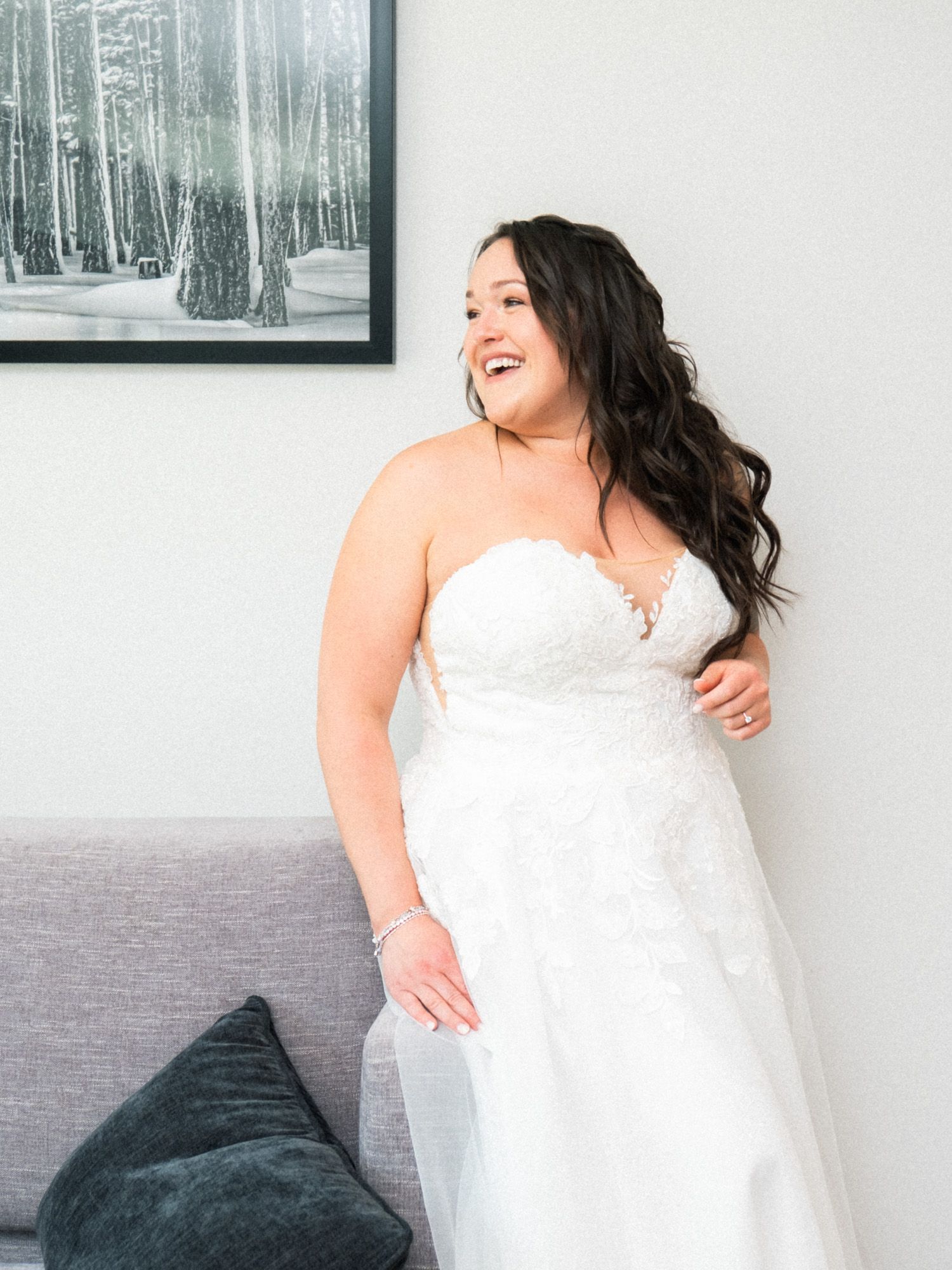 A figure in a white dress poses against a grey backdrop with black and white forest artwork on the wall.