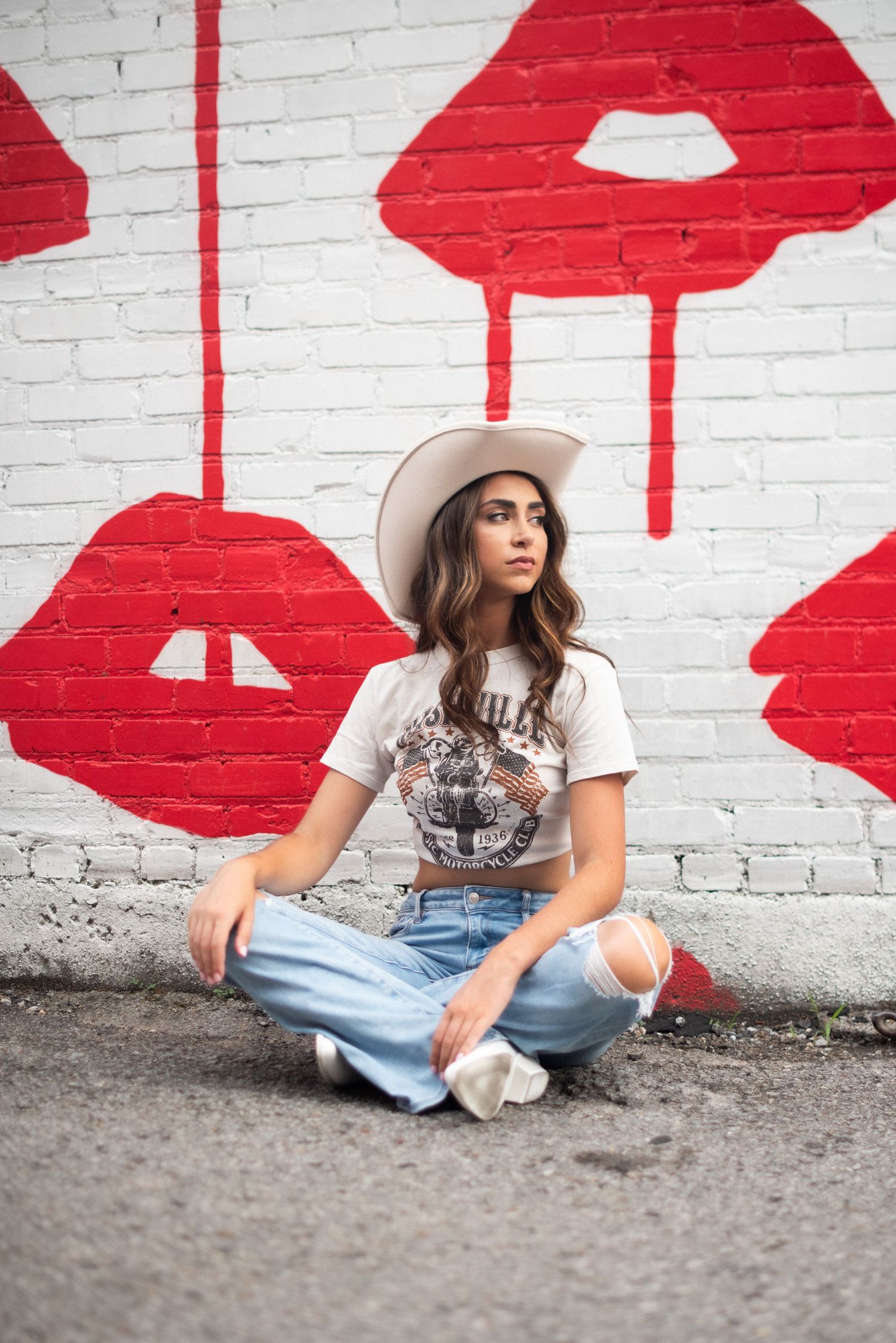 Fashion portrait against white brick wall with red lip pattern wearing denim and wide brim hat.