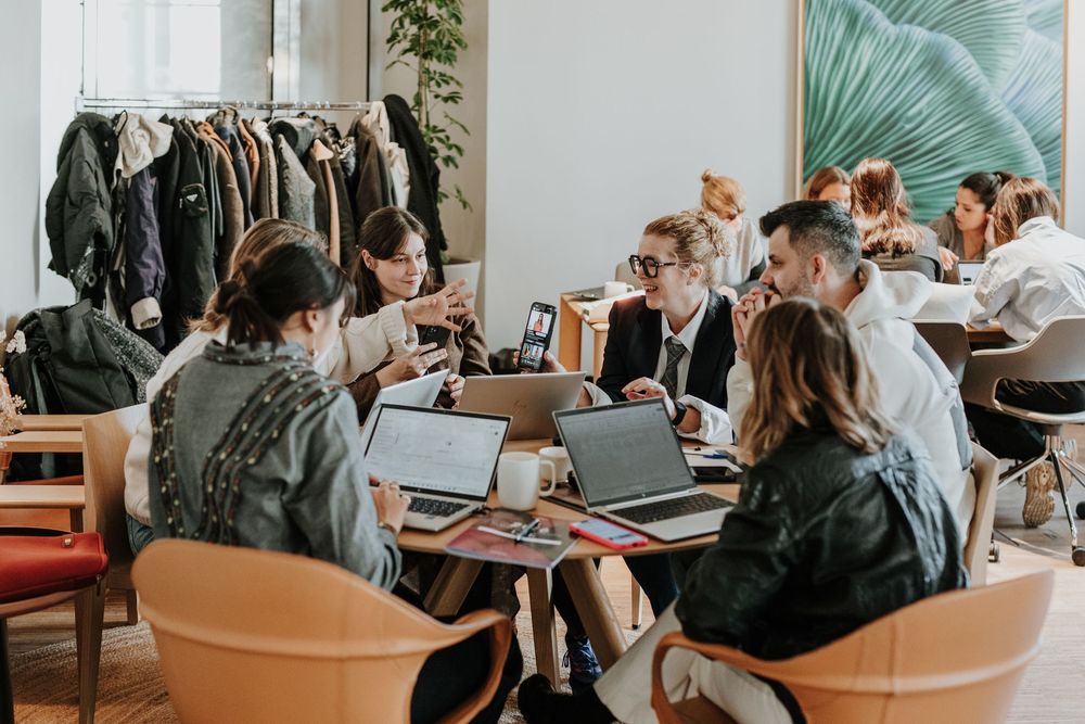 People working together at a modern office space with laptops and documents on shared tables.