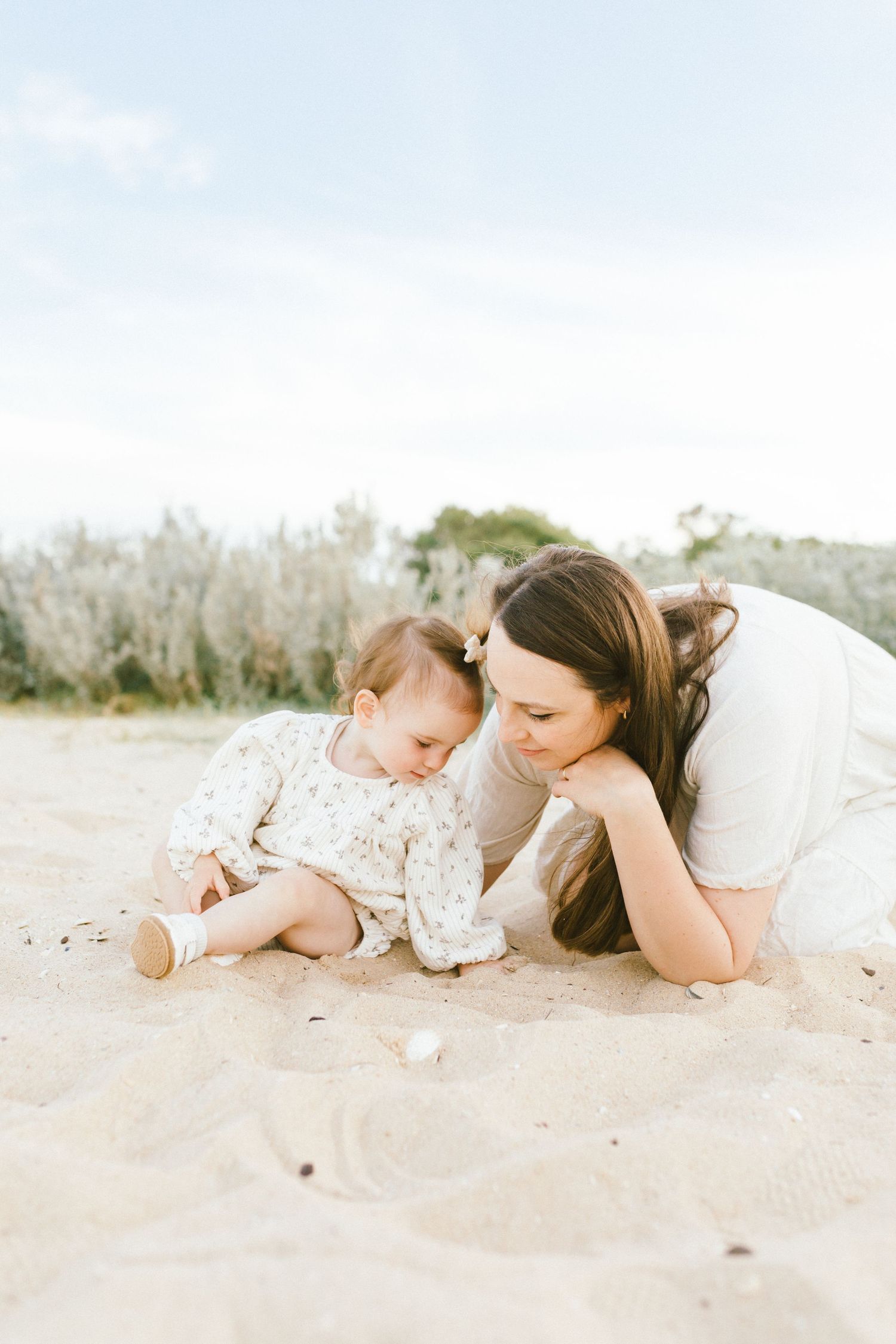 A parent and baby lying together on white sand beach wearing matching floral outfits in a series of tender moments.
