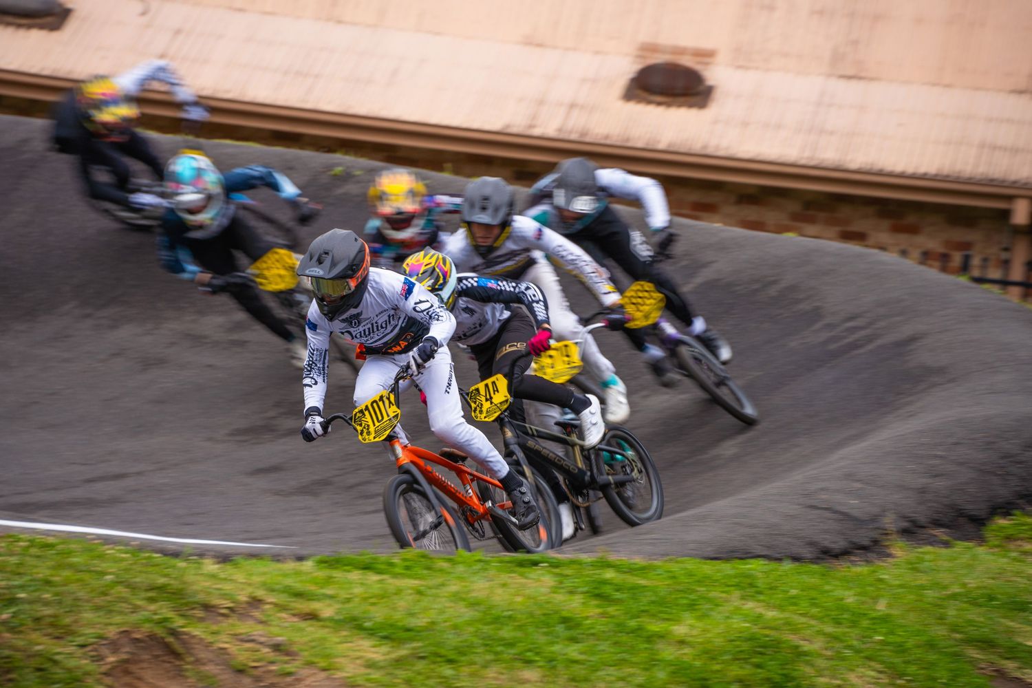 Group of BMX racers competing on a banked dirt track turn.