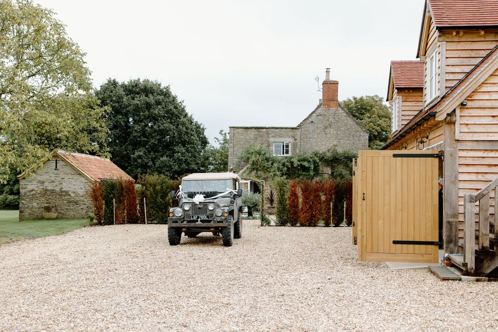 Vintage Land Rover parked in gravel driveway of rustic country house.