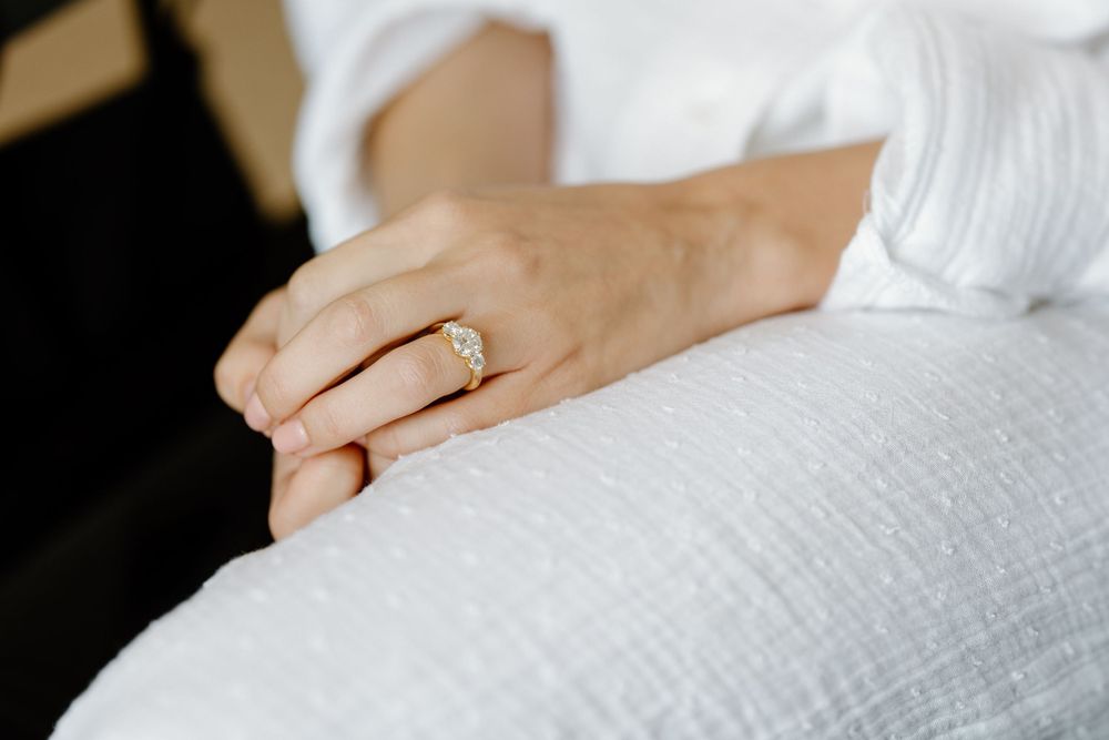 Close-up shot of an engagement ring on a hand resting against white fabric.