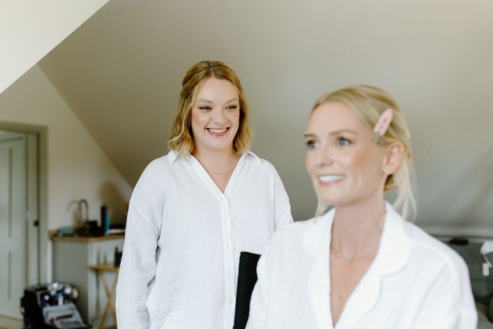 Two women in white robes getting ready for a special occasion in a bright room.