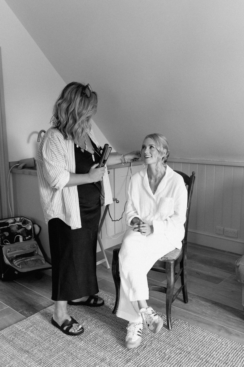 Black and white photo of styling preparation with one person seated while another stands.