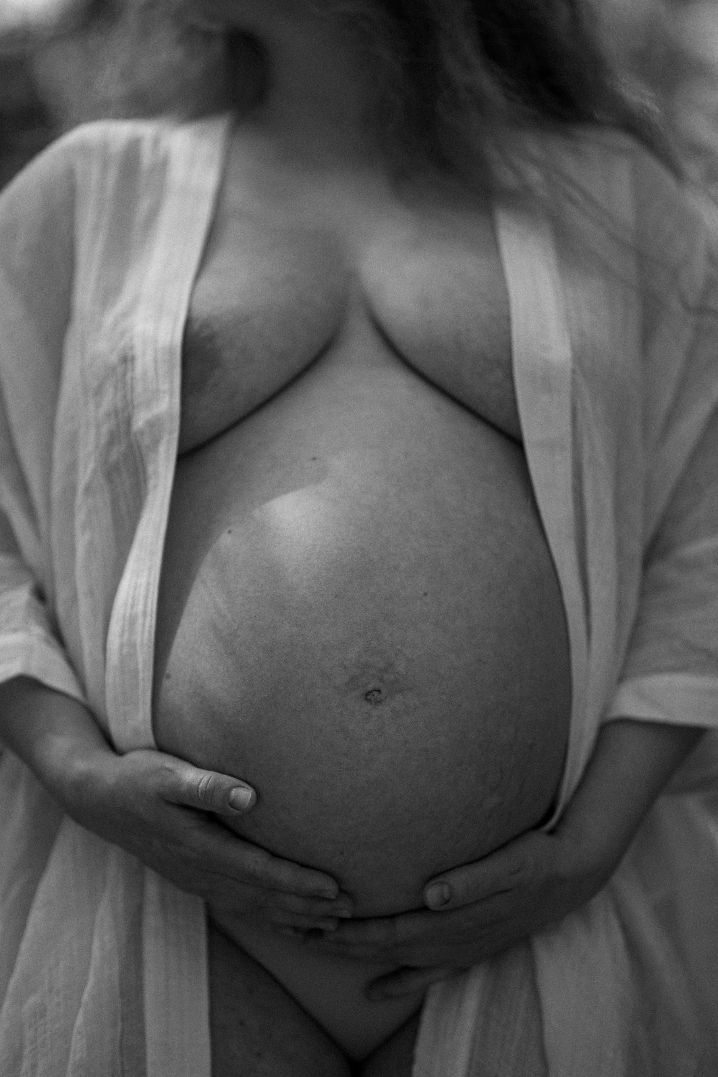 En gravid kvinna i vit öppen kimono håller händerna under sin mage.