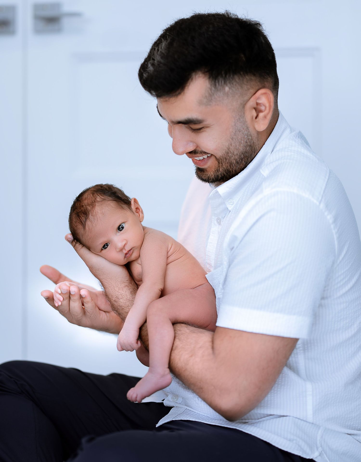 A person in a white polo shirt tenderly holds and gazes at a newborn baby in a bright indoor setting.