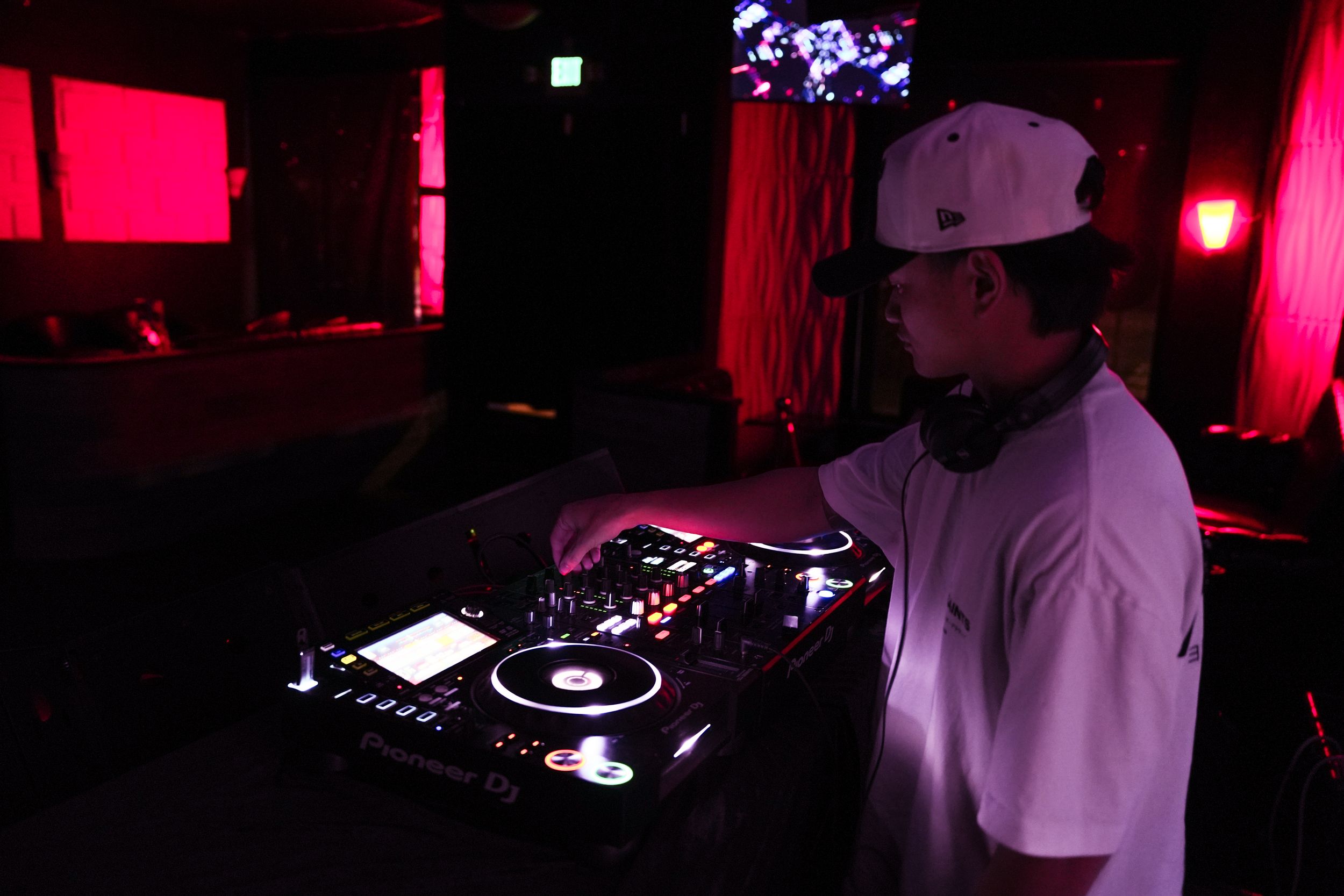 DJ performs at a nightclub using turntables and mixing equipment in a dimly lit room with red ambient lighting.
