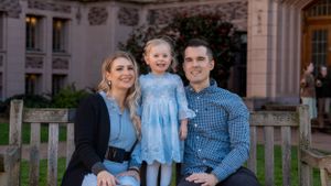 Family of three sitting together on wooden bench in front of ornate building.