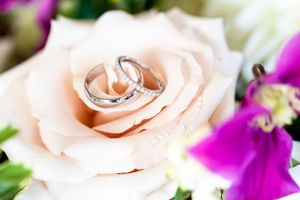 Wedding rings nestled in soft pink rose petals with purple flowers.