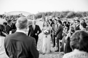 Wedding ceremony takes place on a sandy beach with guests gathered to witness the special moment.