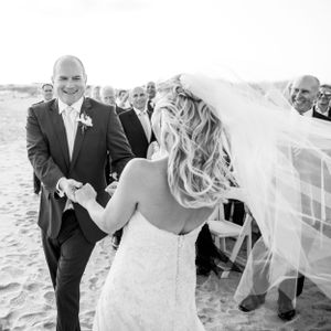 A joyful beach wedding ceremony moment with a strapless lace dress and flowing veil in black and white.