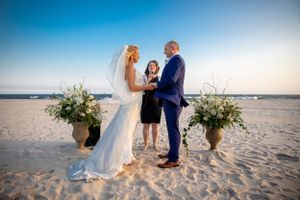 Beautiful beach wedding ceremony at sunset with floral arrangements in sandy coastal setting.