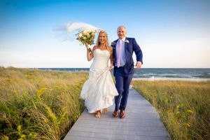 Wedding celebration on a rustic wooden boardwalk by the beach with ocean and dunes in background.