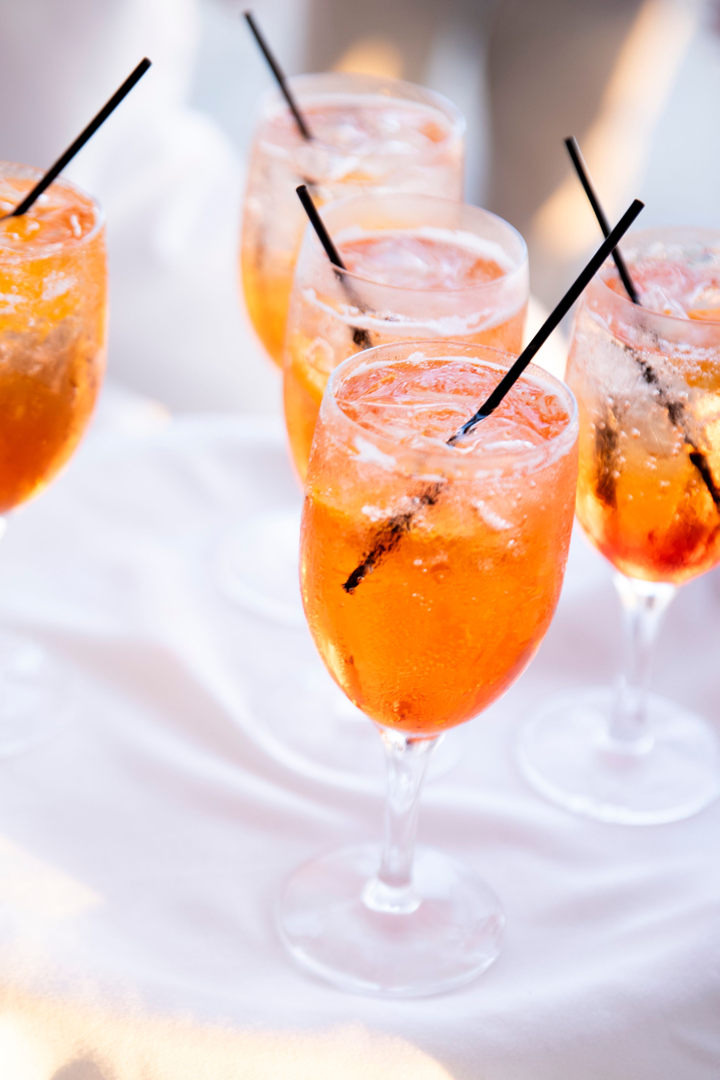 Orange cocktails with black straws served in wine glasses against a white background.