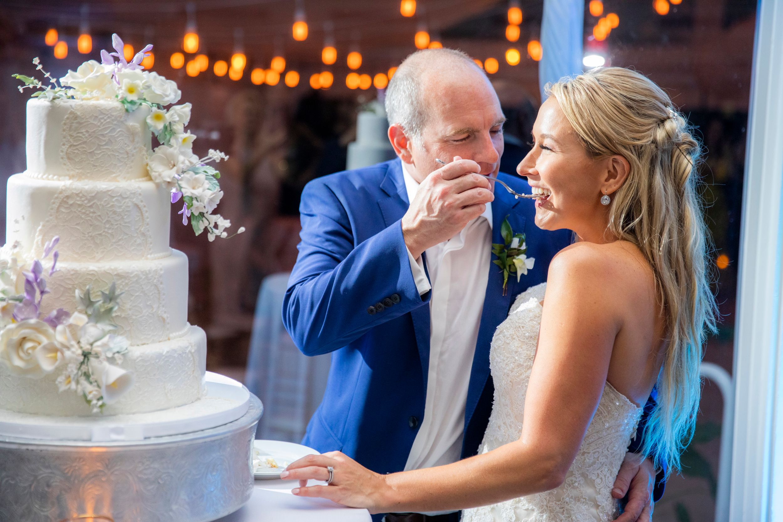 Wedding couple shares a moment of joy while cutting their floral-decorated wedding cake.