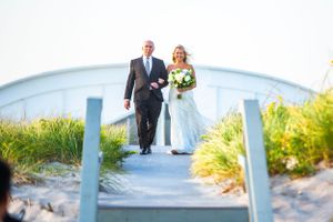 Wedding couple walking down blue-railed boardwalk steps near the ocean.