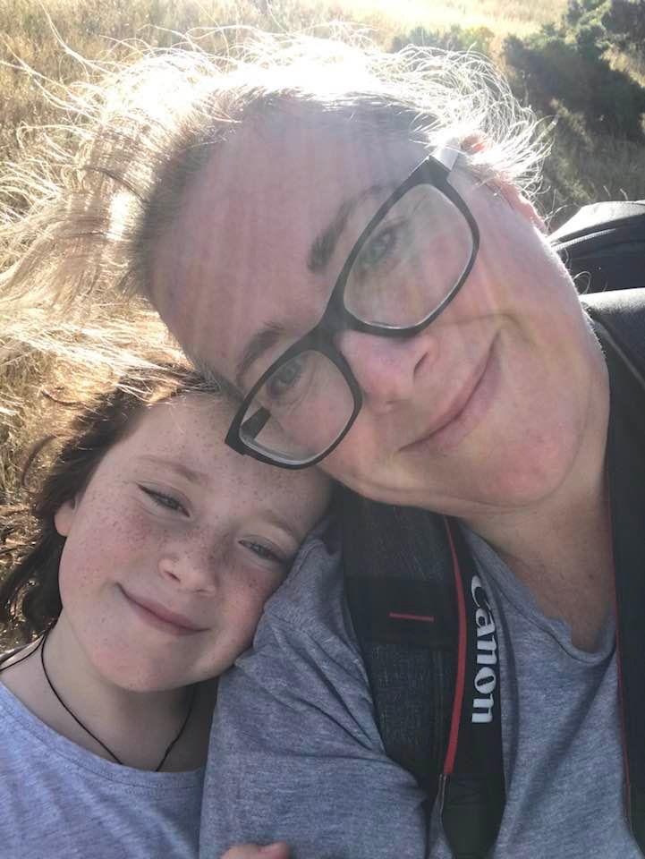 Selfie of a woman and her daughter looking at the camera with light shining behind their heads.