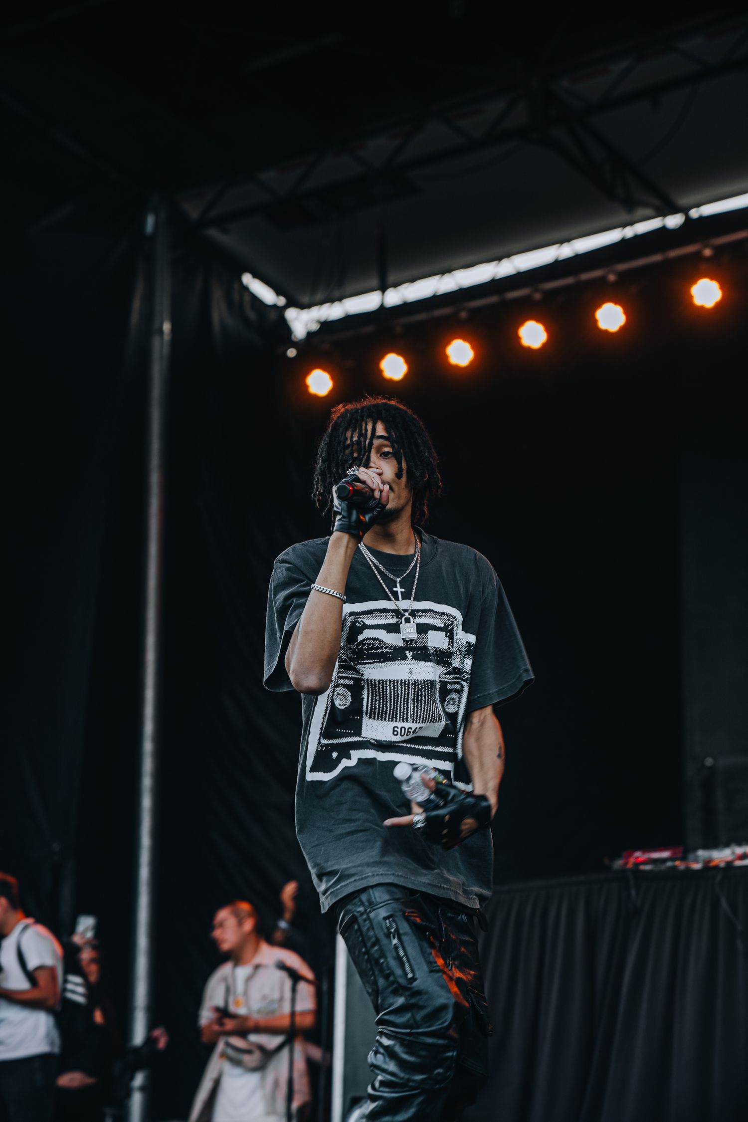 A performer in casual streetwear delivers an energetic performance on an outdoor festival stage.