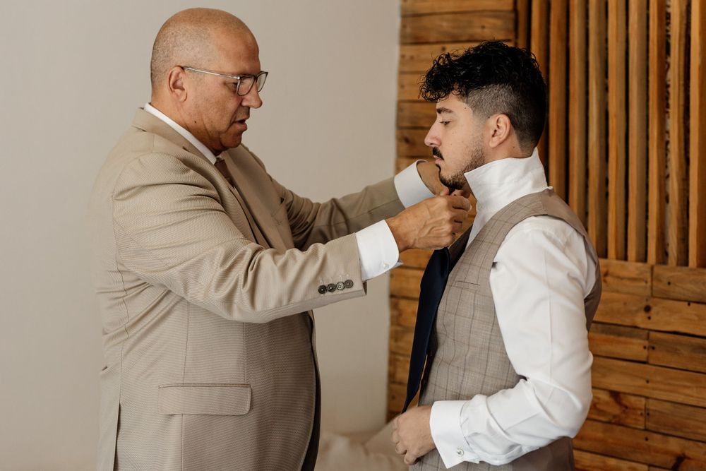 Two people share a touching moment while adjusting formal attire.
