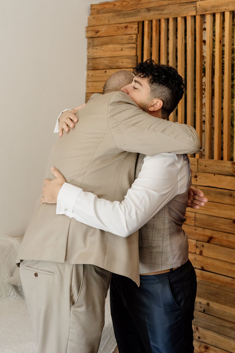Two people sharing an emotional embrace in formal attire against a wooden panel wall.
