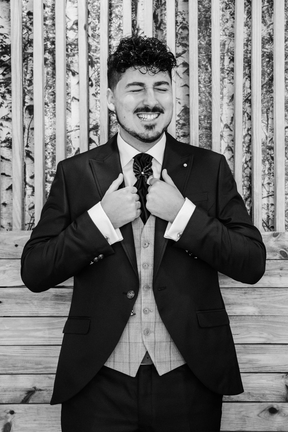 A formal portrait of someone adjusting their tie while smiling against a striped background.