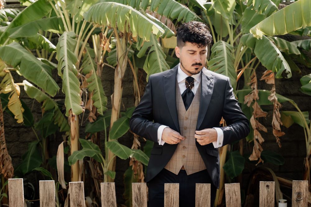 Formal portrait of someone in a suit and tie posing in front of tropical foliage.