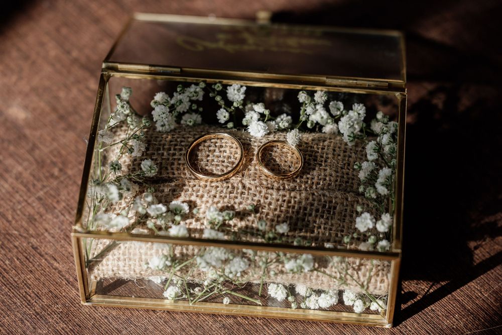 Wedding rings displayed in a glass box filled with delicate baby's breath flowers on burlap.